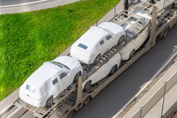 Transportation of new cars covered with protective fabric tarp on a truck trailer